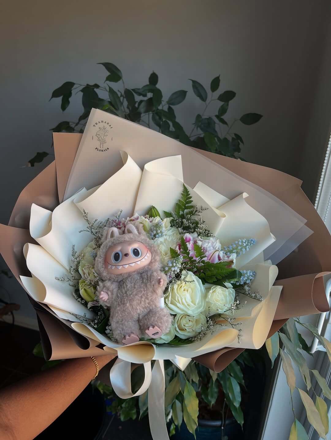  Ein Labubu-Plüschtier in einem Blumenstrauß, was seine Beliebtheit als Geschenkidee unterstreicht.
