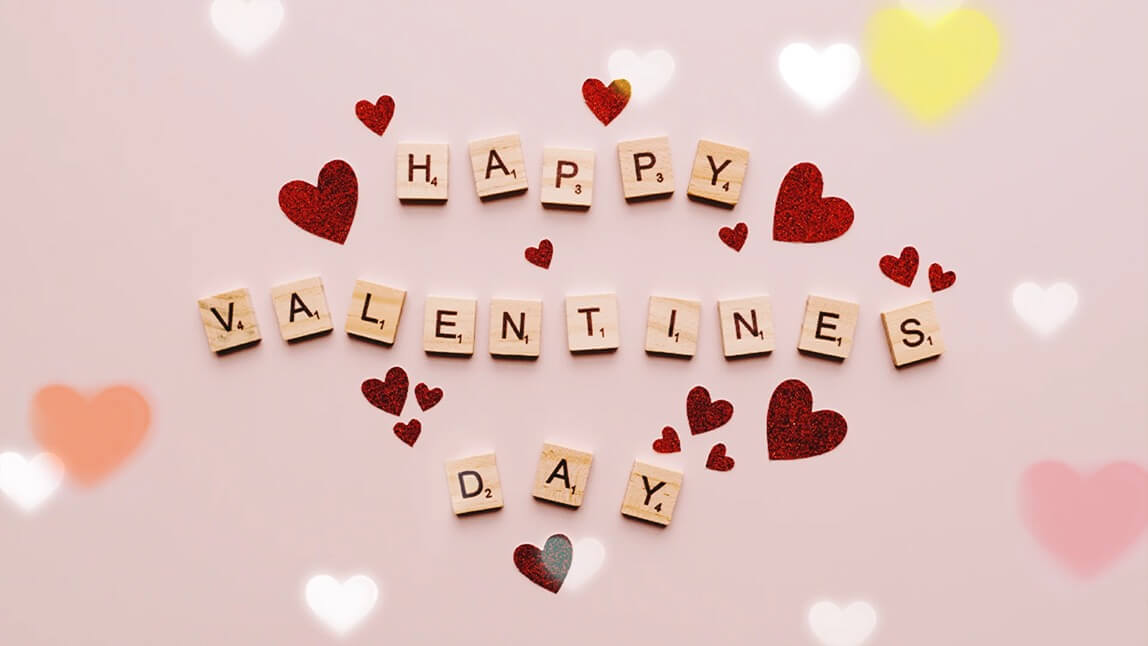 Happy Valentines Day Schriftzug aus Scrabble-Buchstaben mit roten Glitzerherzen auf rosa Hintergrund