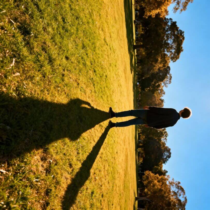 Silhouette einer Person im Park bei Sonnenlicht, langer Schatten fällt in unlogische Richtung, grüne Wiese