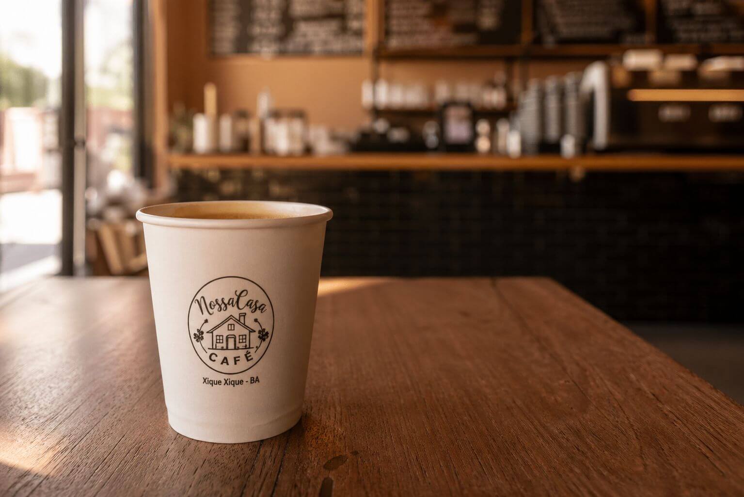 Mockup fotorealista de um copo de café de papel com logotipo sobre uma mesa de madeira rústica em uma cafeteria, criado com IA.
