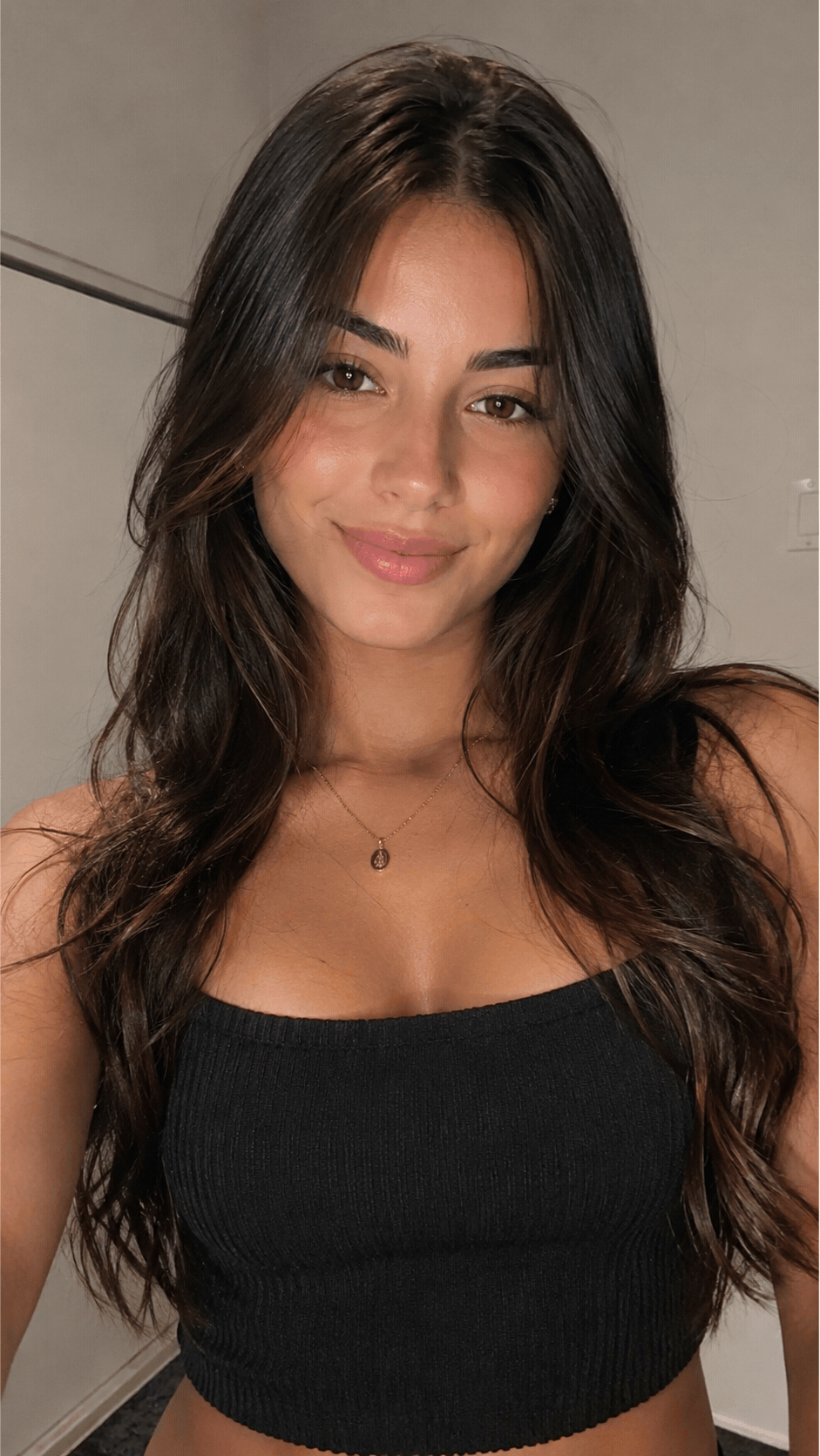 Selfie de mulher com cabelo escuro e blusa preta, iluminada por flash direto.