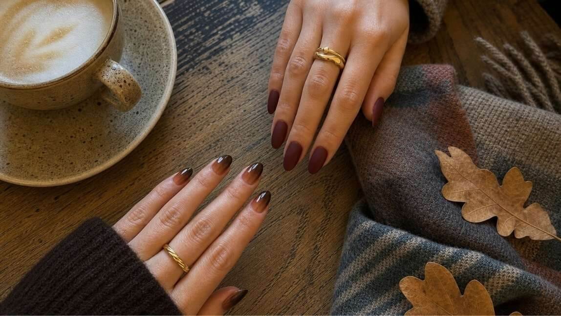 Zwei Hände mit herbstlichem Nageldesign in Schokobraun und Warm Vanilla Latte French auf einem Holztisch mit Kaffee und Herbstlaub