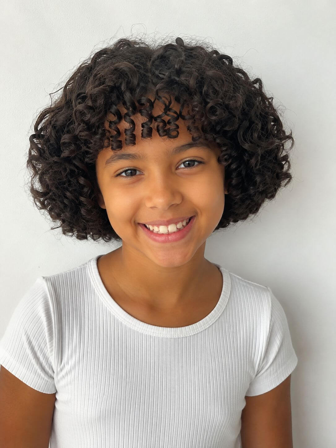 Menina com corte infantil para cabelo cacheado, formato arredondado, volume equilibrado e franja cacheada.