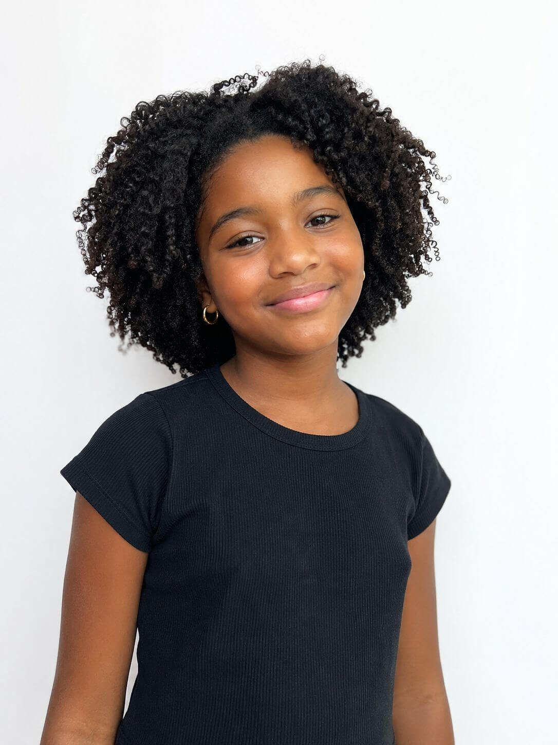Menina negra com cabelo crespo infantil natural, volume cheio e corte arredondado em camadas suaves.