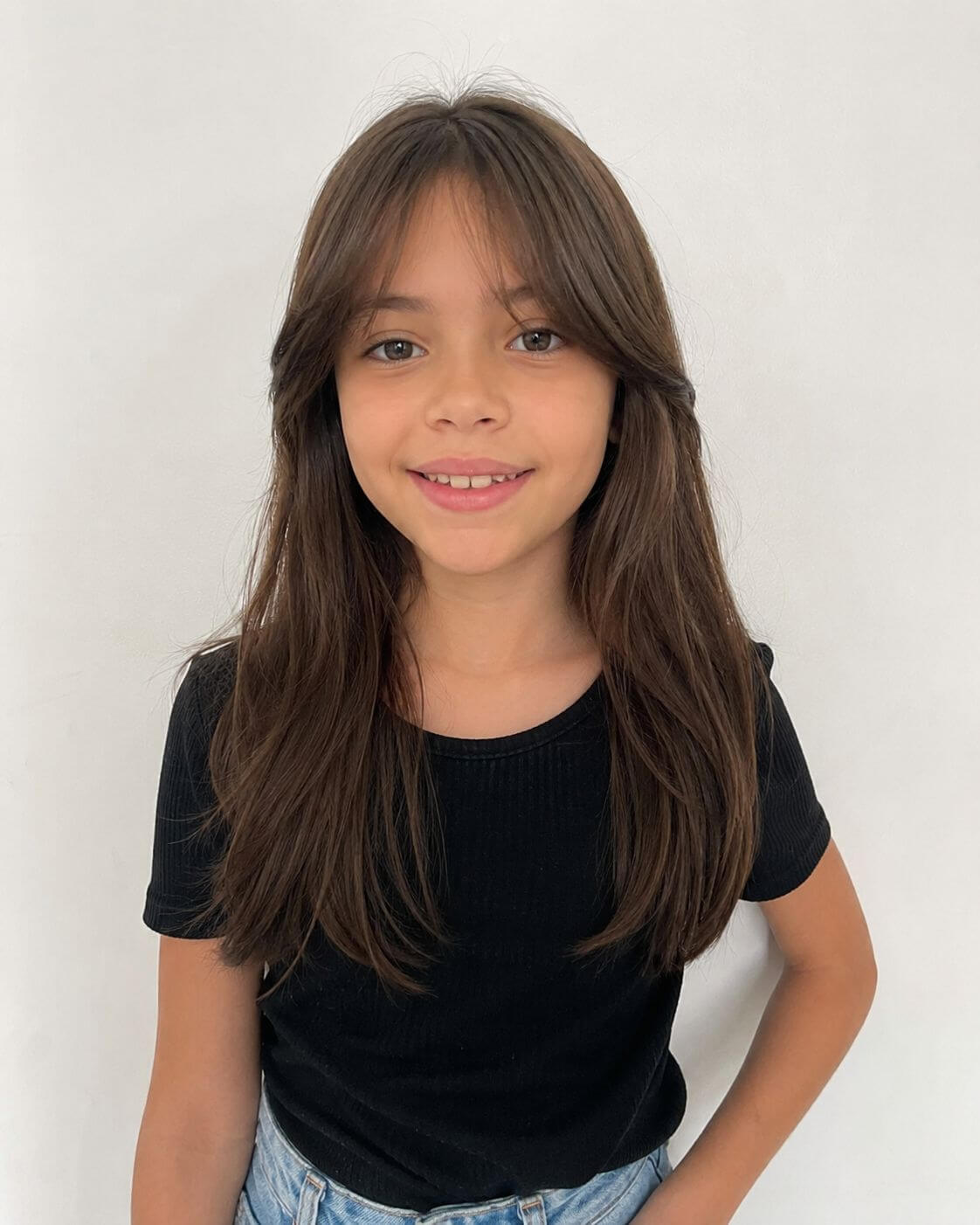 Menina com cabelo longo e franja cortininha, dividida ao meio e integrada às camadas frontais.