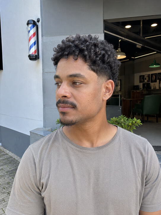 Homem brasileiro com corte taper fade cacheado e cachos definidos no topo