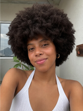 Mulher negra com black power arredondado e cabelo crespo volumoso