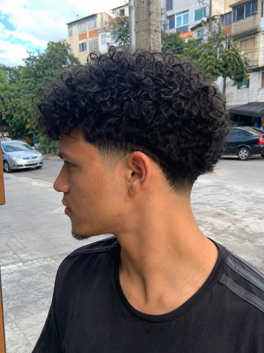 Homem brasileiro com corte americano cacheado e degradê médio nas laterais