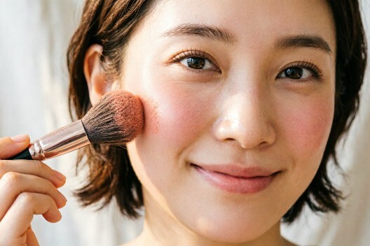 Applying blush to the apples of the cheeks with a fluffy brush