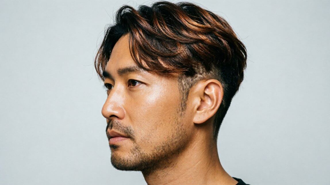 Close-up side profile of a man's warrior cut showing long flowing top layers contrasted with short faded sides