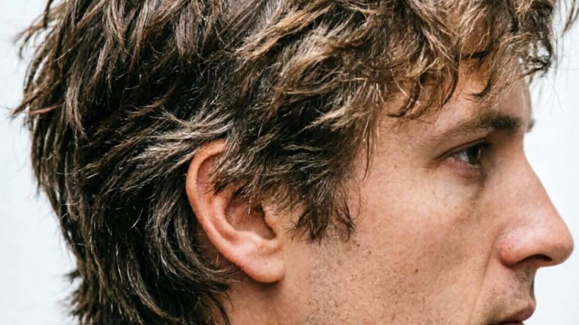 Close-up photorealistic side profile of a man's shag haircut showing heavily layered, feathered ends and textured crown,