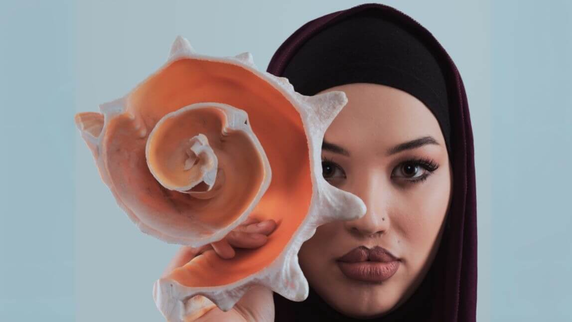 A woman in a hijab gently holds a large shell, showcasing its intricate details and natural beauty.