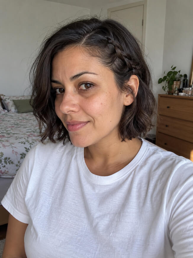Mulher com cabelo curto ondulado e pequena trança frontal presa atrás da orelha.