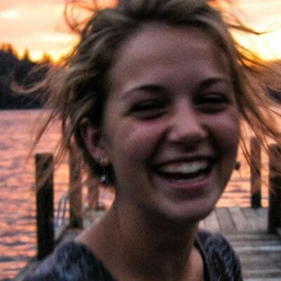 Close-up of a blurry, low-detail old phone photo of a smiling woman at a lake at sunset
