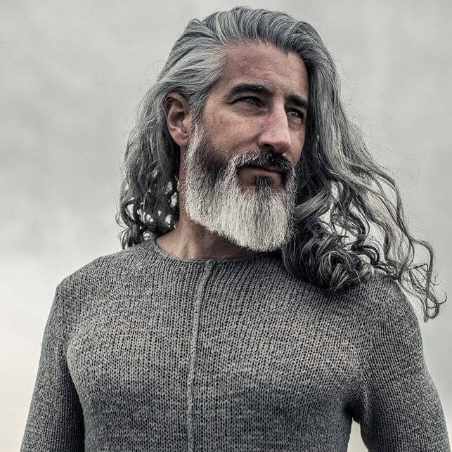 Mann mit sehr langem, grauem Haar und vollem weißen Bart, getragen in natürlichen Wellen, markanter und individueller Langhaar-Stil.