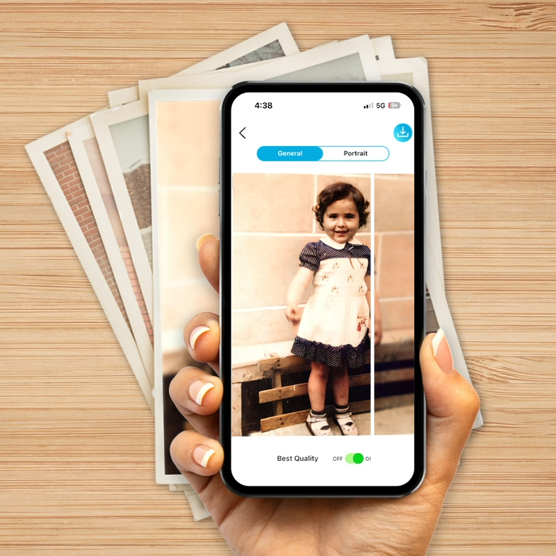 Hand hält ein Smartphone, das die digitale Restaurierung eines alten Kinderfotos zeigt. Im Hintergrund liegen weitere analoge Fotos. Ideal für die Suche nach Möglichkeiten, alte Fotos digitalisieren zu lassen.
