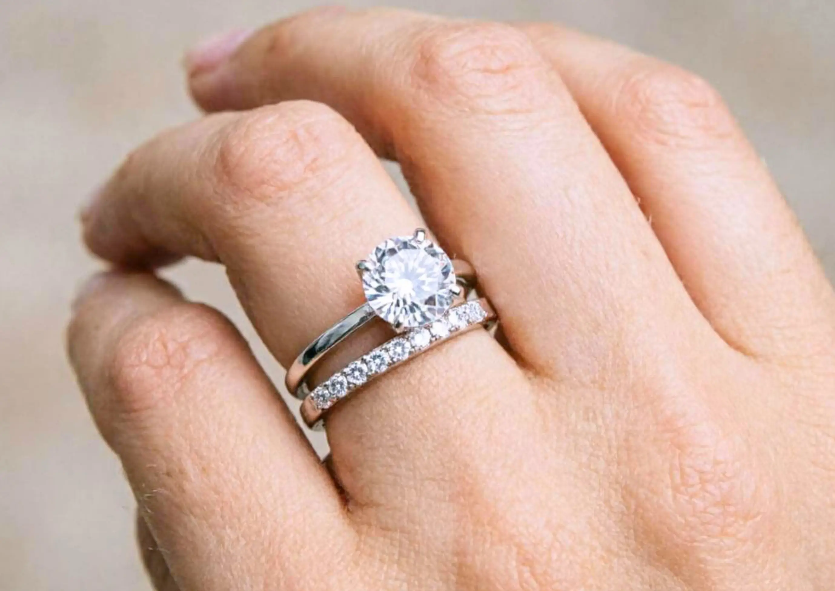 Hand wearing a stacked combination of a 1.5 carat diamond engagement ring and a matching diamond wedding band