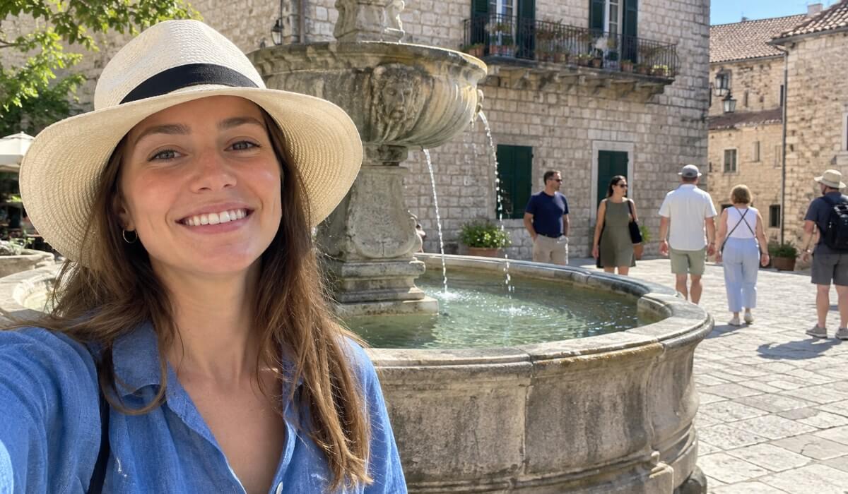 Selfie by a stone fountain with five tourists walking in the background